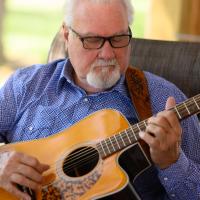 Ronnie looks at his guitar intently as he strums it.