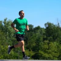 Ryan runs outside. He is wearing a green shirt, black shorts, and tennis shoes.