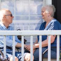 A photo of Carol and Rick posing for the camera while sitting together on their porch.