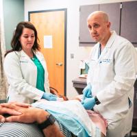 Dr. O’Donnell and his assistant examine Todd's knee while he lies down on an examination bed.