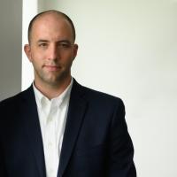 Dr. Phillip Almeter, a middle-aged white man with very short hair, stands inside the Kroger Field stadium in front of a white background. He is wearing a black suit and a white shirt.