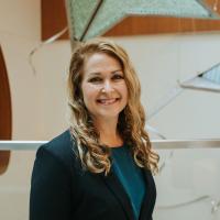 Dr. Lindsay Ragsdale, a white woman with medium-length curly blonde hair, smiles for the camera. She is wearing a black blazer over a teal top.