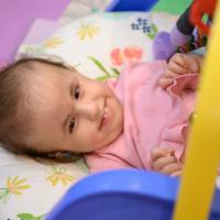 Wylie is laying on a cushion and smiling as she looks up at a baby mobile.