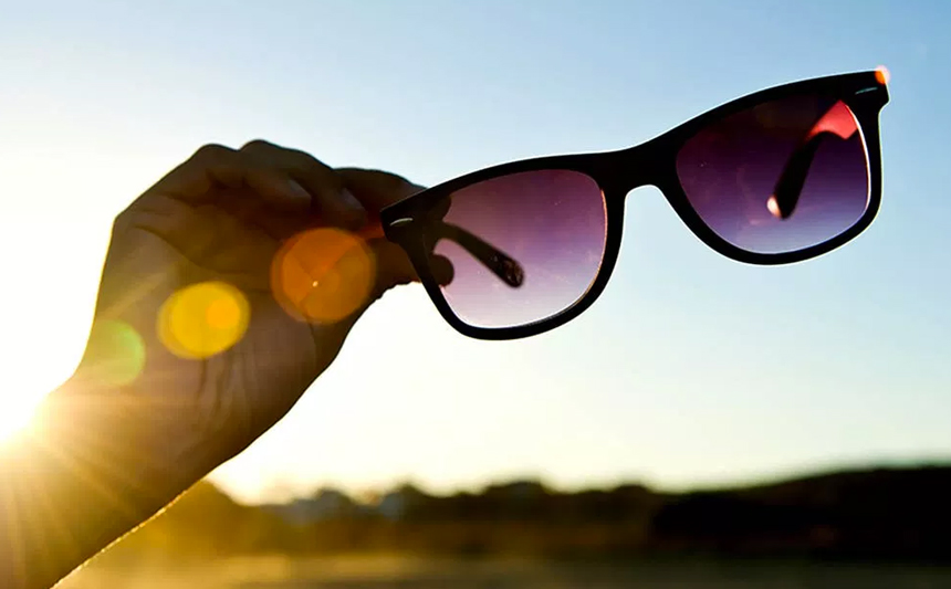 A pair of sunglasses are held up to the sky.