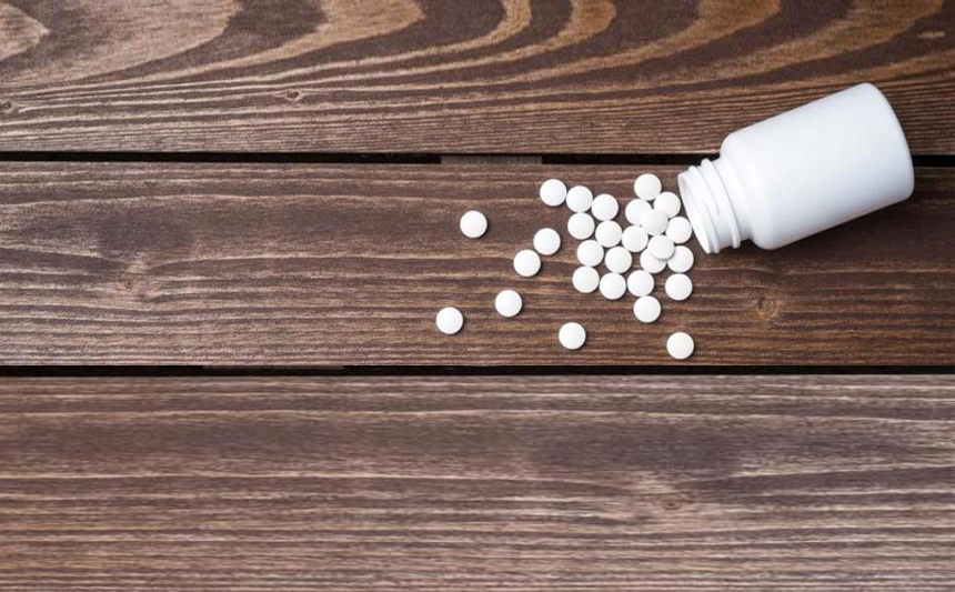 A bottle of white tablets are spilled on a wooden table.