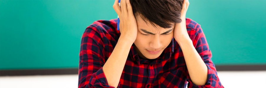 A teenaged boy with a headache presses his hands to his temples.