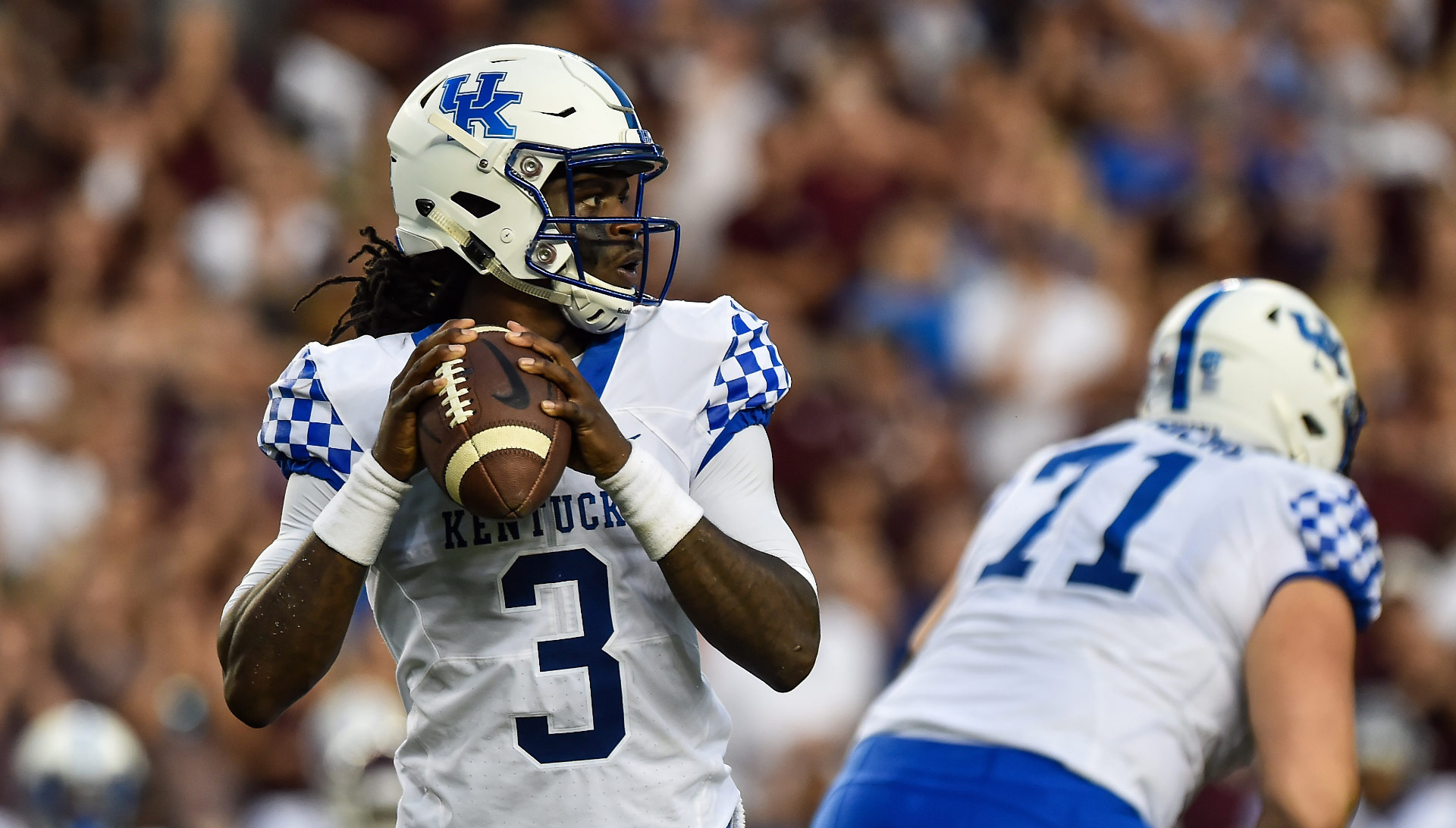 An action shot of Terry Wilson, a young, athletic Black man dressed in his football uniform and helmet, preparing to throw a football during a University of Kentucky game.