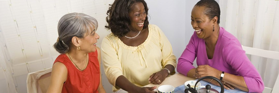 Three women laugh and talk while having tea.