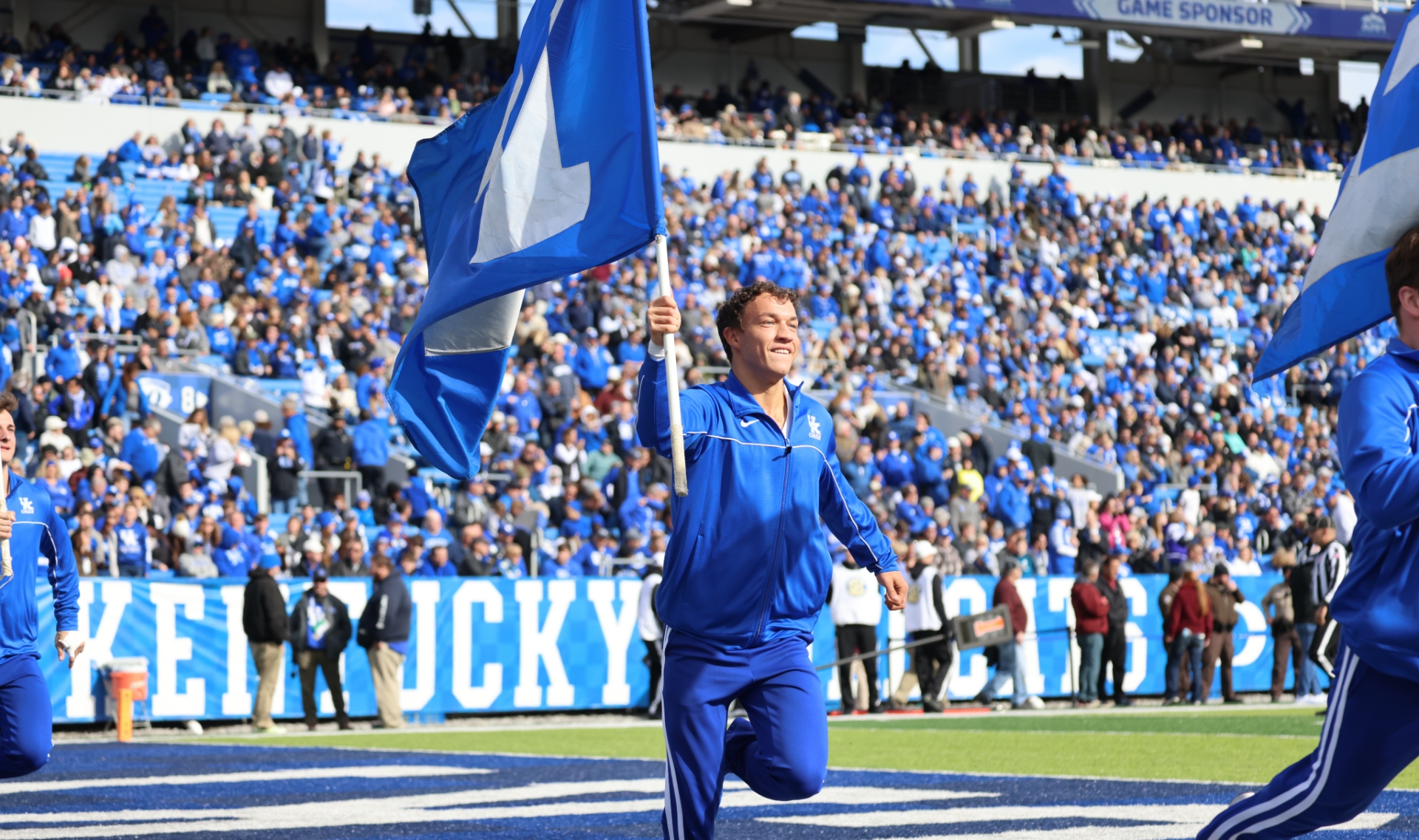 An action shot of Travis running while holding a UK flag at a football game.