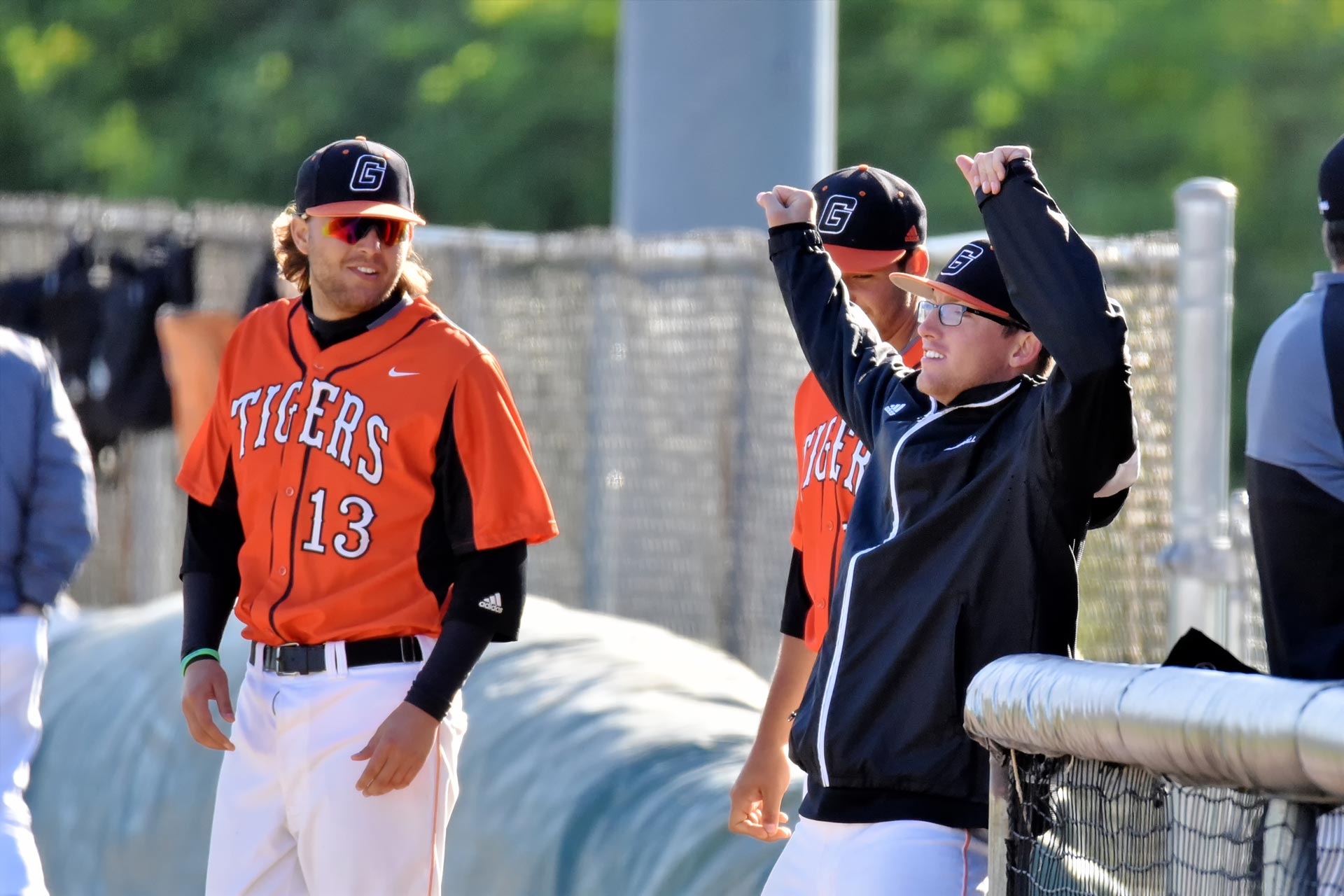 Trent looks to his teammate and gives him a half smile. They are standing on a baseball field in their Tigers baseball uniform and caps.