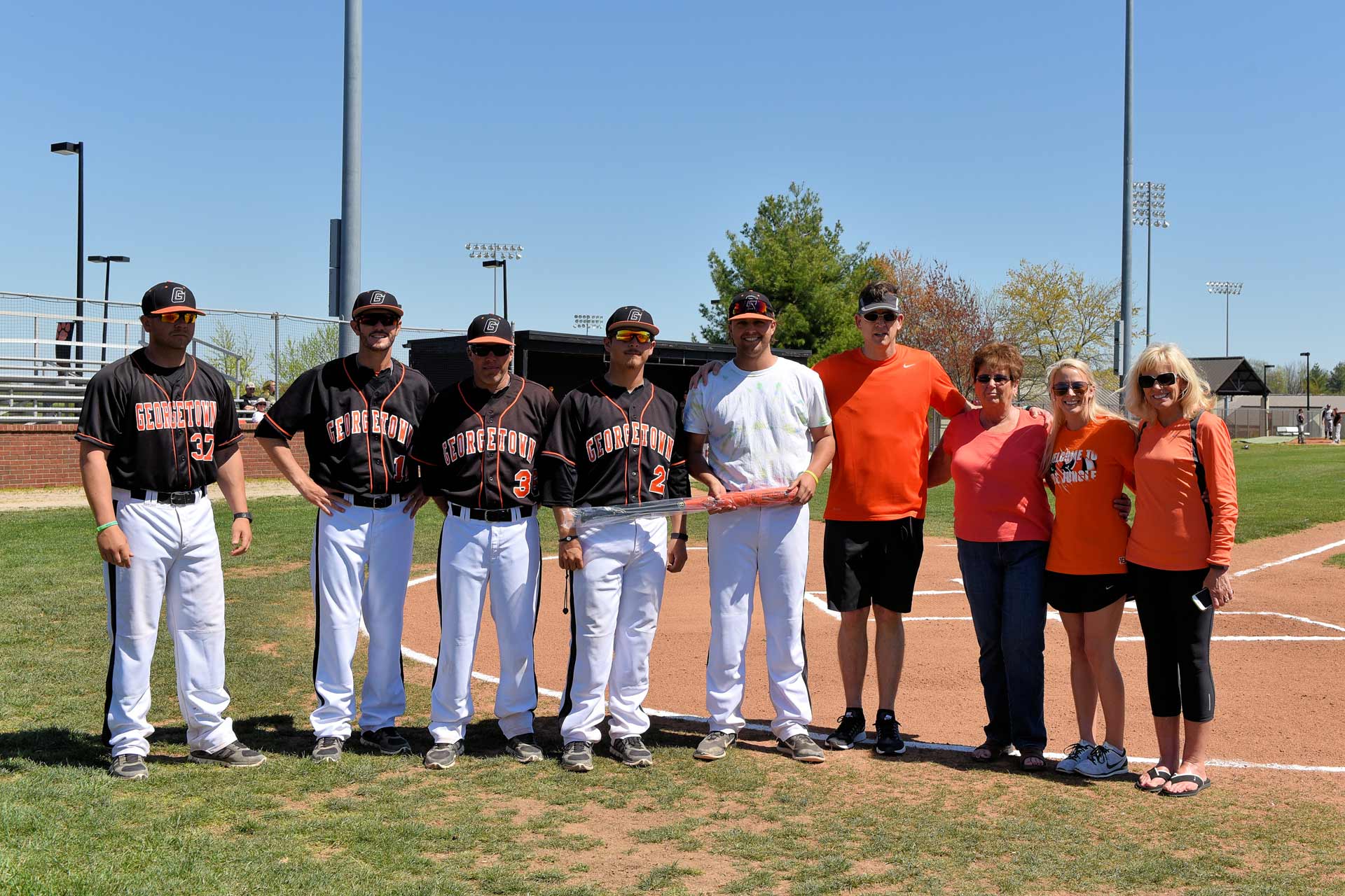 Trent poses for a photo on a baseball field, surrounded by his teammates and his family members, holding a baseball bat.
