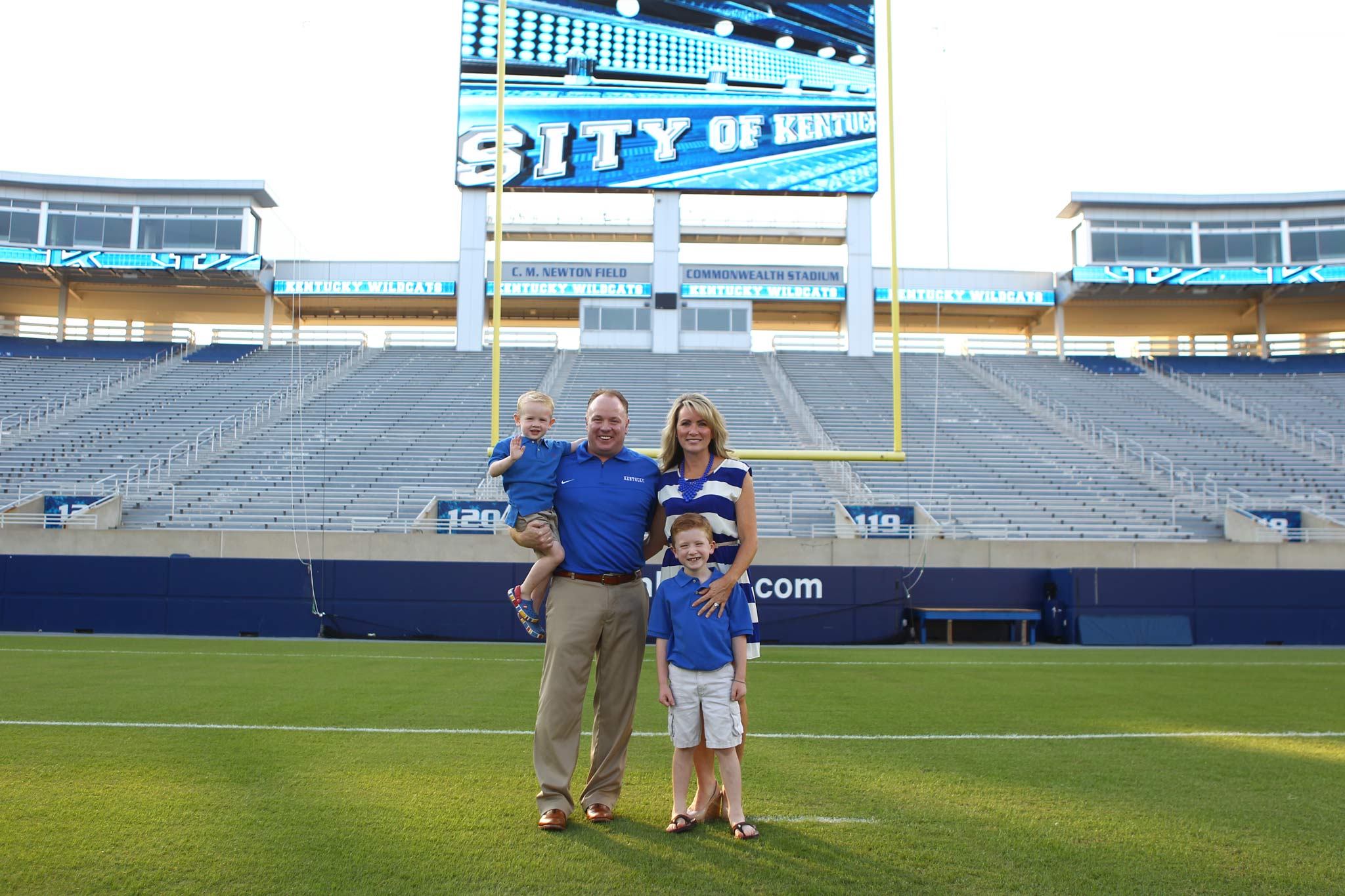 Coach Stoops stands with his wife and sons in front of the goal at Kroger Field. They are all wearing blue.