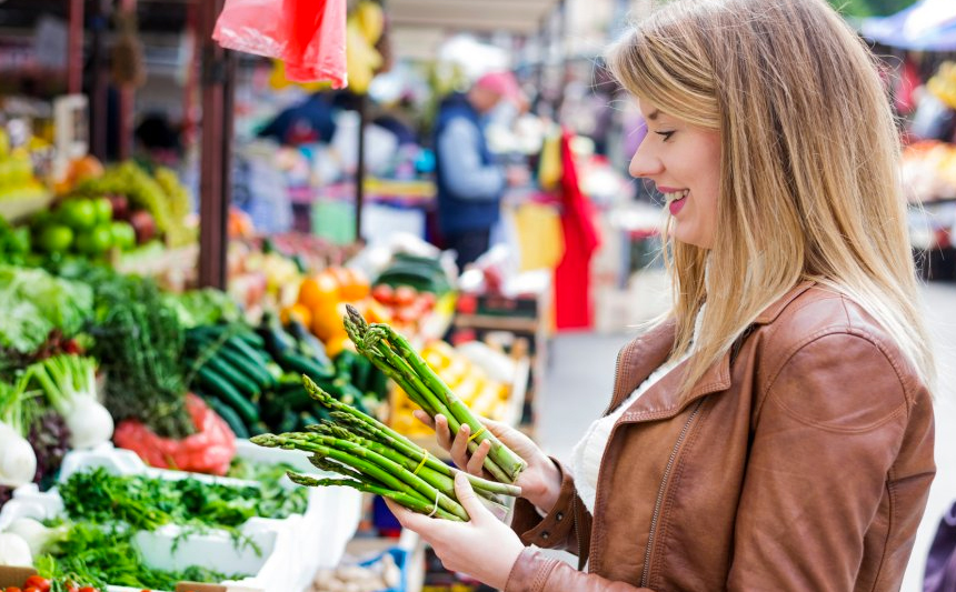 A woman examines asparagus at an outdoor farmers market.