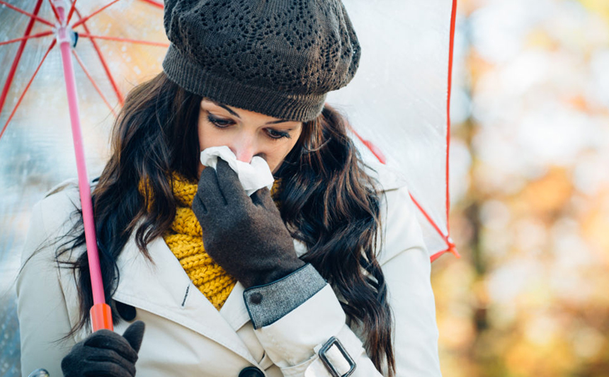 A warmly dressed woman with an umbrella blows her nose.