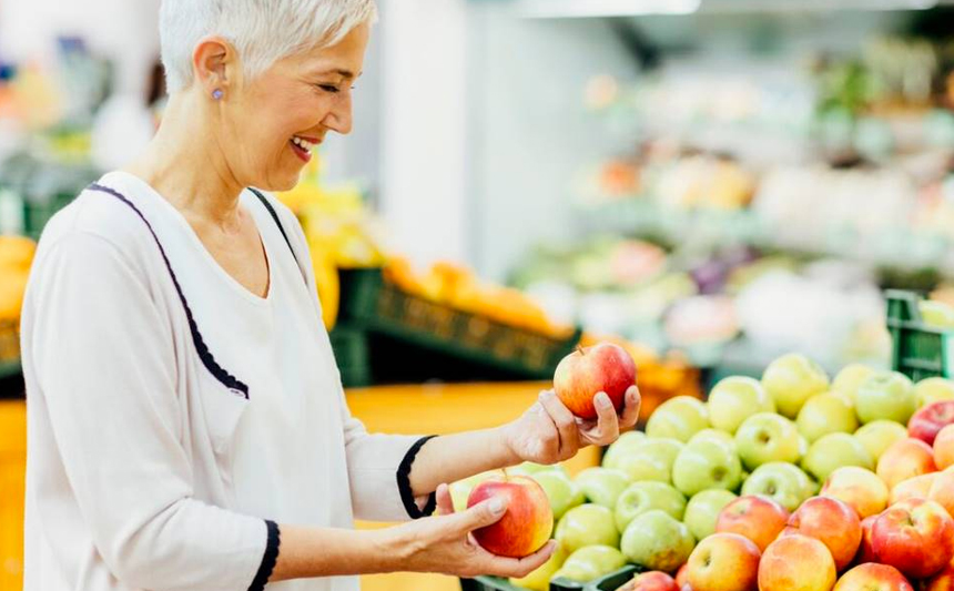 A woman examines an apple in the produce section of a grocery store.